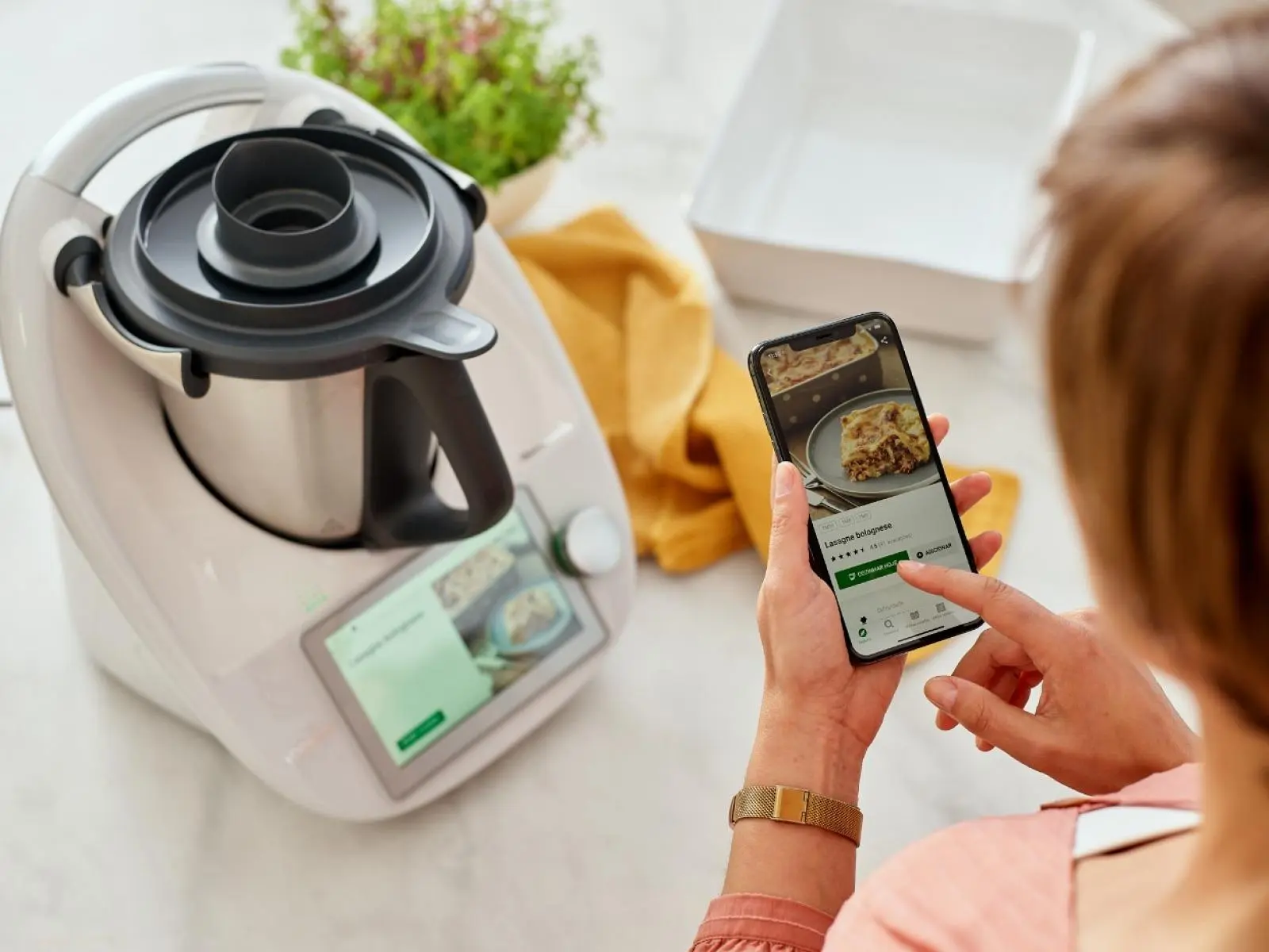 Haushaltsgerät mit Touchscreen neben einem Smartphone, das ein Rezept anzeigt, auf Küchenarbeitsplatte.
