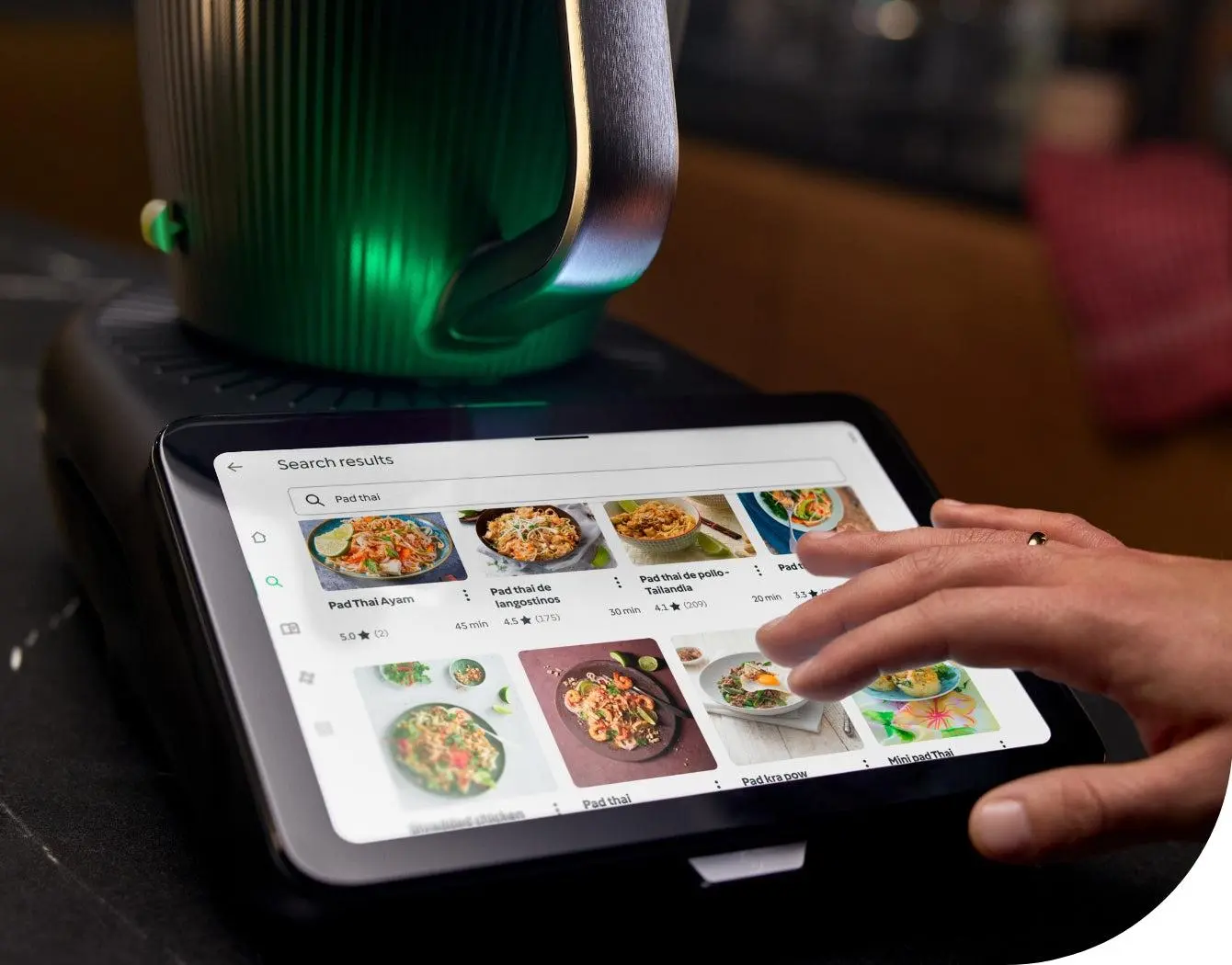 Tablet mit Rezeptvorschlägen auf einem Tisch, daneben grüner Staubabsaugpinsel und Thermomix-Topteil im Hintergrund.