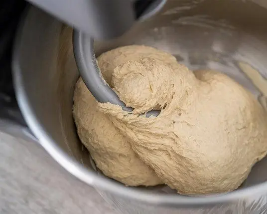 Teigkneten in einer Küchenmaschine mit beigefarbenem Hefeteig in Edelstahlschüssel.